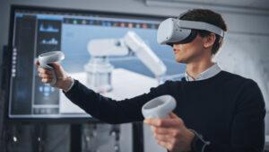 Studentischer Ingenieur mit Virtual-Reality-Headset, der Joysticks hält und bionische Gliedmaßen steuert, während Aktionen auf dem Bildschirm angezeigt werden.