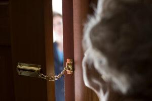 Ältere Frau mit einer Sicherheitskette an der Haustür, draußen steht ein Fremder