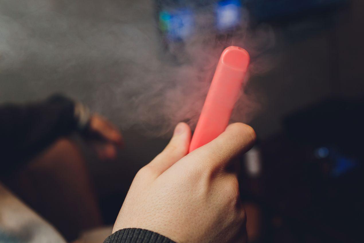 Hand hält eine pinkfarbene Einweg E-Zigarette ähnlich der Elf Bar 800 mit aufsteigendem Dampf