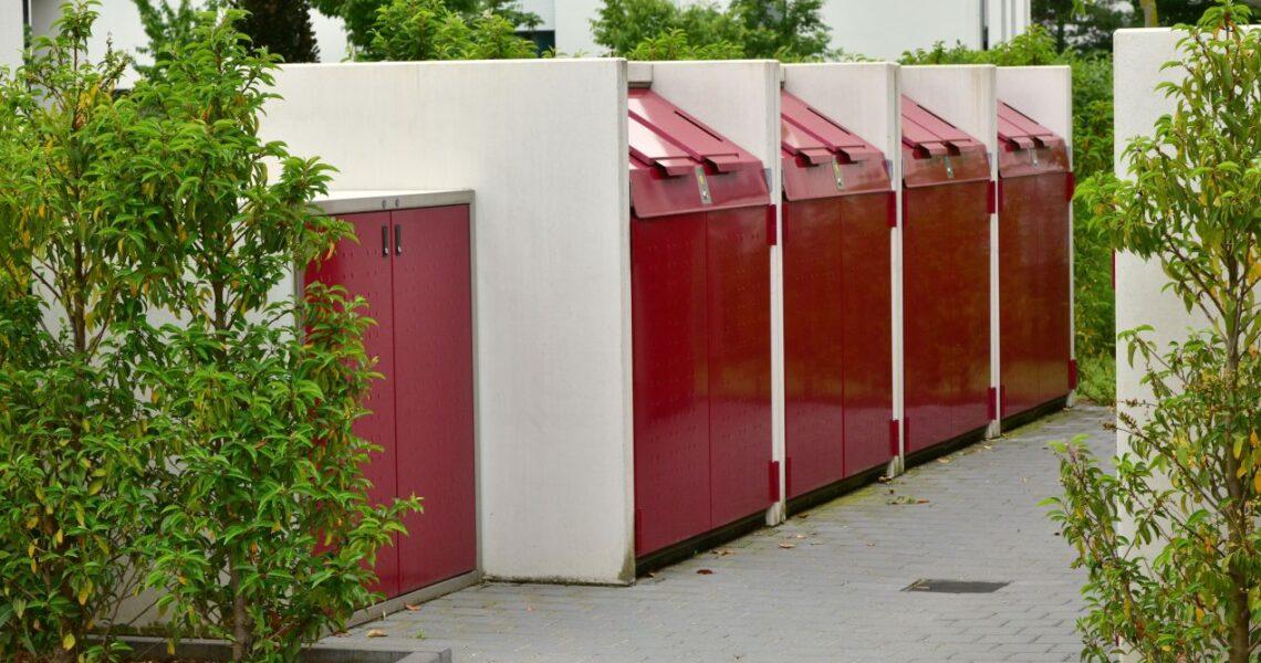 Muelleinhausung aus Beton und Metall mit roten Klappen in einer gepflegten Wohnsiedlung