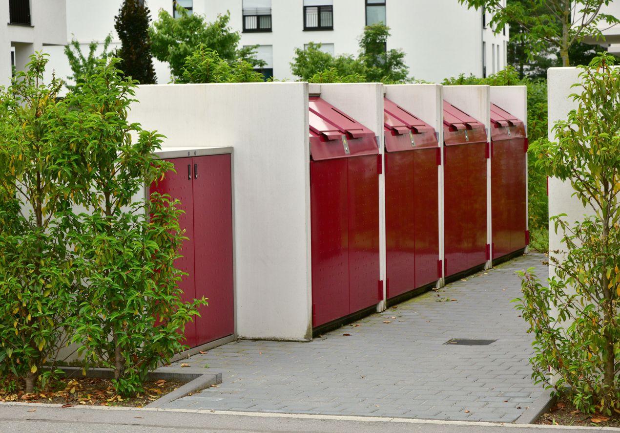 Muelleinhausung aus Beton und Metall mit roten Klappen in einer gepflegten Wohnsiedlung