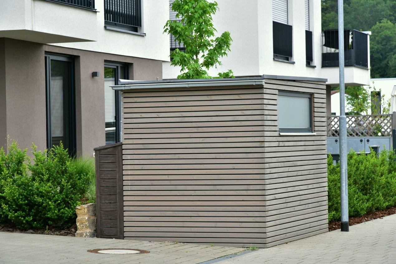 Muelleinhausung aus horizontalem Holzprofil mit integriertem Fenster vor modernem Wohngebäude