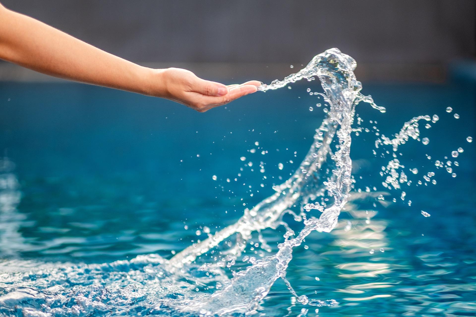 Hand spritzt Wasser im hellblauen Pool | Sandfilteranlage